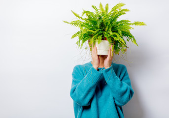 Portrait of a beautiful white smiling woman in blue sweater with fern plant on white background,...