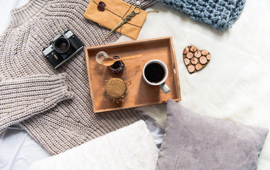 Top view wooden tray with cup of coffee and can of honey. Gadget and envelope locating on sweater. Breakfast concept