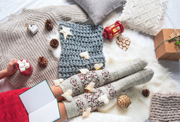 Top view woman legs in warm socks lying on carpet. She tasting beverage and reading volume in room. Leisure concept