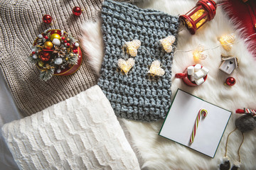 Top view knitted scarf, sketch-book, garland and cup with marshmallow locating on carpet. Winter holiday concept