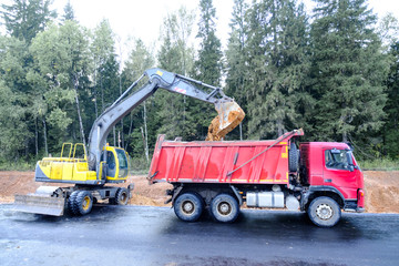 The wheel excavator loads the earth with a bucket to the body of a multi-ton dump truck on the...