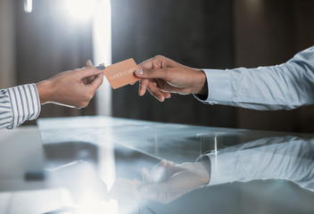 Close up of male and female hands while he is giving privileged personal card to her. Guy is checking-in at reception desk and paying for service