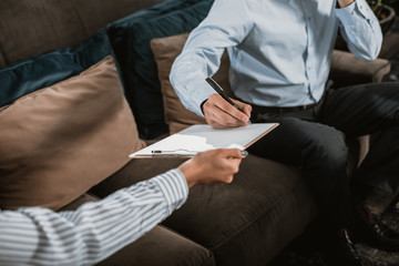 Fototapeta premium Close up of male and female hands transferring clipboard with sheet of paper. Lady is giving it to businessman while he is writing on it with pen