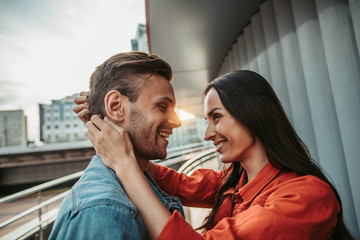 Side view beaming girl embracing outgoing man while talking with him. They having leisure outdoor
