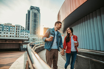 Smiling man telling with cheerful girl while tasting mugs of delicious liquid during relax outdoor....