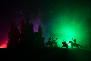 Medieval battle scene with cavalry and infantry. Silhouettes of figures as separate objects, fight between warriors on dark toned foggy background with medieval castle. Night scene. Selective focus
