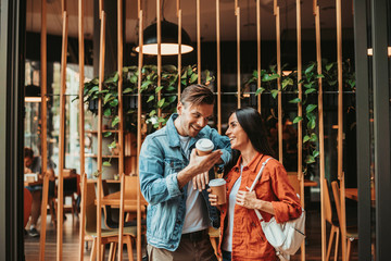 Positive male talking with laughing woman while tasting cups of coffee near cafe. They...
