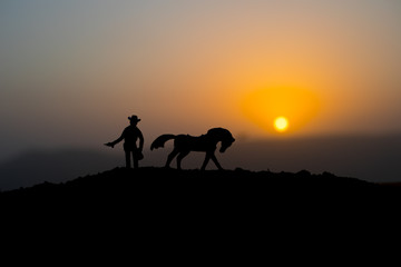 Fototapeta na wymiar Cowboy concept. Silhouette of Cowboys at sunset time. A cowboy silhouette on a mountain with an yellow sky.