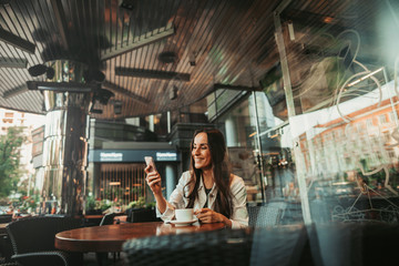 Fototapeta na wymiar Portrait of happy woman talking on digital device while tasting mug of appetizing coffee during relax inside