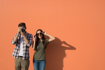 Portrait of cheerful man taking photo on contemporary camera while standing near positive lady in sunglasses during leisure. Copy space