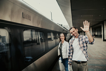 Portrait of outgoing male gesticulating hands while holding lady arm before journey. They looking...