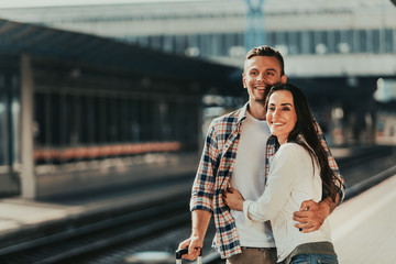 Fototapeta premium Portrait of beaming woman embracing positive male while standing on railway station during sunny day
