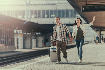 Full length portrait of happy man and concerned girl gesticulating hands while walking on platform with baggage