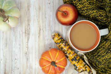 Cozy fall autumn background with coffee cup, indian corn, pumpkins, apple and a warm blanket. Room for copy space on wood background
