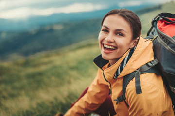Delighted young woman resting on the slopes of the mountain while feeling happy - obrazy, fototapety, plakaty