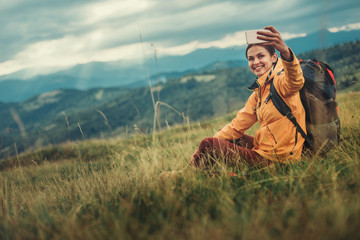 Positive attractive young woman sitting on the mountain hill while making panorama photos
