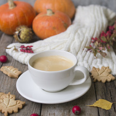 Coffee cup, knitted scarf, dry leaves, cookies, pumpkin, chestnuts, hawthorn and barberry fruits on a wooden background. Concept cozy atmosphere with a cup of coffee. Copy space, selective focus