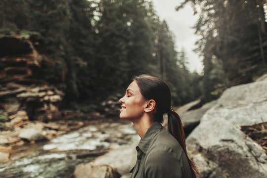 Positive nice young woman smiling while standing in the forest and breathing fresh air