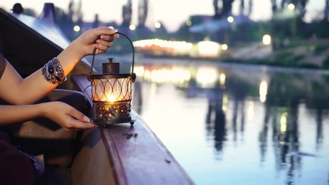 hands of a girl are holding a decorative lantern on a boat in a river near the bank