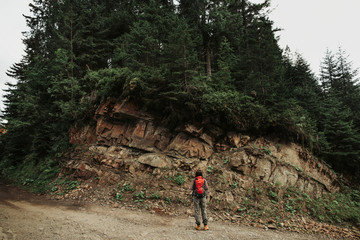 Beauty of nature. Full length back view portrait of girl with backpack standing on the road and observing hillside in the forest