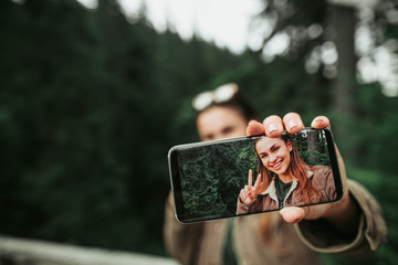 Look at me. Close up of mobile phone with photo of smiling girl in female hand. Woman and green...