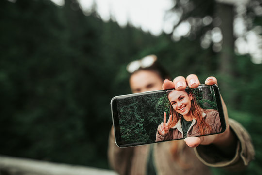 Look at me. Close up of mobile phone with photo of smiling girl in female hand. Woman and green forest on blurred background