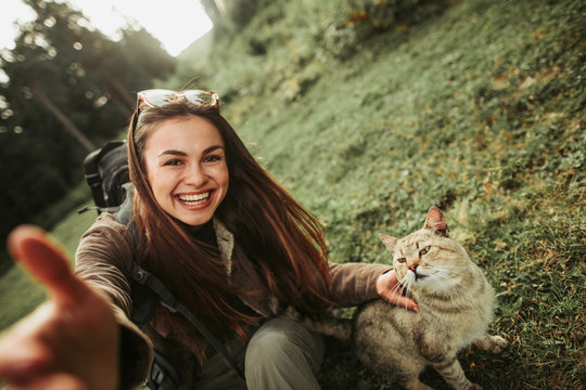 My four-legged friend. Portrait of charming young lady with backpack taking photo with fluffy pet. She is looking at camera with wide smile