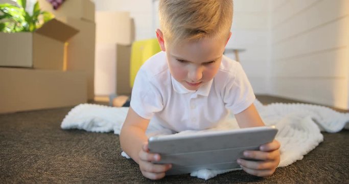 Boy using digital tablet while lying on floor at new home, carton boxes background.