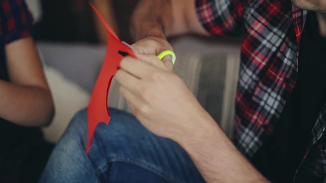 man is cutting heart from colored paper by scissors on Valentine's Day near sweetheart