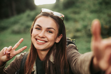 Happy moment. Close up portrait of beautiful smiling girl taking photo and showing peace gesture....