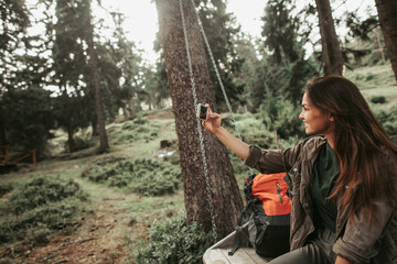 I want to remember this day. Portrait of charming girl taking photo with smartphone while sitting on wooden swing. She is smiling