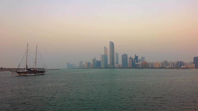 Beautiful shot of Abu Dhabi city skyline towers and beach at sunset - Big wooden boat at the beach
