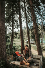 Fototapeta premium My favorite song. Portrait of beautiful girl sitting on wooden bench among trees. She is listening music on smartphone and smiling