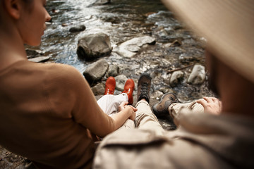 Couple relaxing. Peaceful young woman thoughtfully looking at the water while holding hands with her boyfriend and sitting next to the river