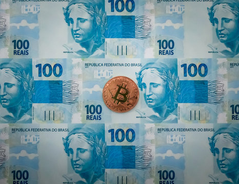 Criptomoeda Bitcoin bronze em cima de notas de cem reais