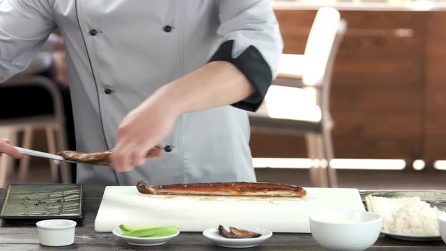Chef cutting smoked fish. Man in uniform preparing food.