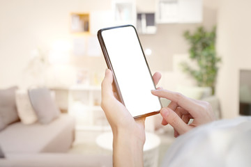 Female hand holding blank screen mobile smart phone over living room. - Powered by Adobe