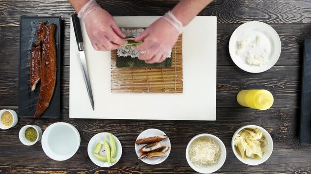 Hands making food, sushi roll. Cream cheese, avocado and eel.