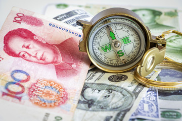 Defective compass placed on the dollar and yuan banknotes. The concept of direction of financial or investment at present and in the future.