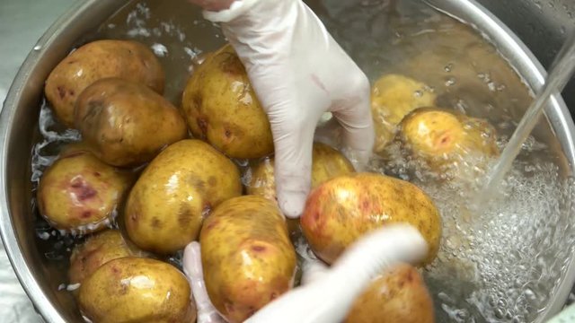 Hands washing potatoes close up. Raw vegetables, bowl with water.