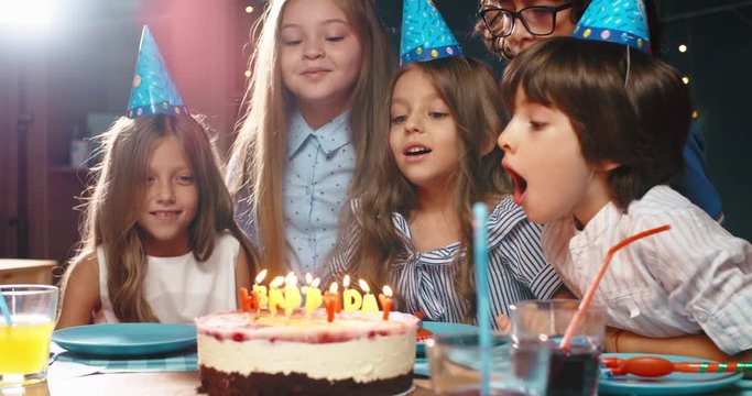 Children celebrating birthday party, blowing out the candles on birthday cake. Group of kids having fun on birthday party - happy childhood concept 4k