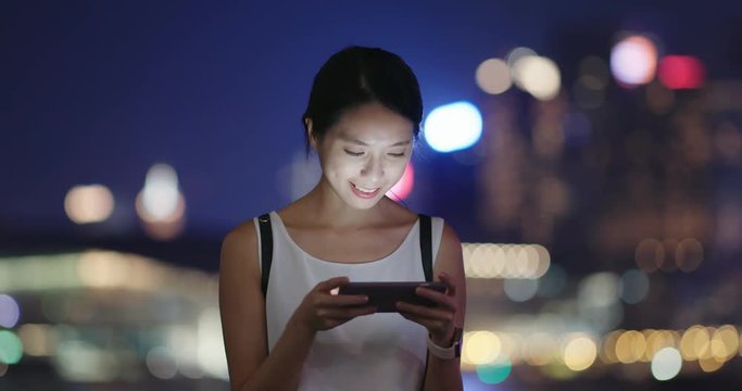 Woman play game on cellphone in city at night