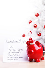 Piggy bank and a Christmas budget plan in front of a white Christmas tree