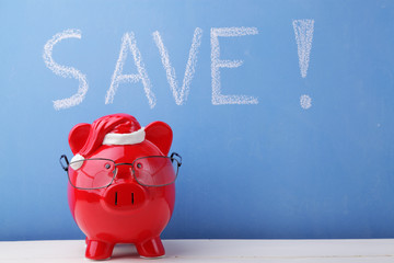 Christmas piggy bank with glasses in front of ablue blackboard where the word "save!" has been written with white chalk.