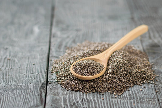 Wooden spoon with black Chia seeds on a dark wooden table.