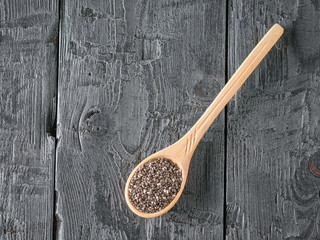 Wooden spoon with black Chia seeds on a dark wooden table. The view from the top. Flat lay.