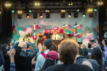 stage at the pop concert, the viewer's hand, raised up, blurred figures of artists with their hands...
