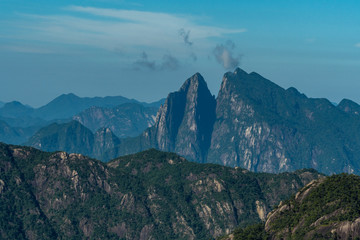 cracked peak at forest covered valley floor under blue hazy at mount sanqing geo park