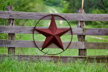 Texas rustic star on countryside side wooden fence, with road to the house slowly dissolving in the...