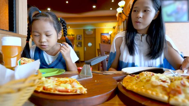 Asian family, mother and daughter eat pizza happily at pizza shop.